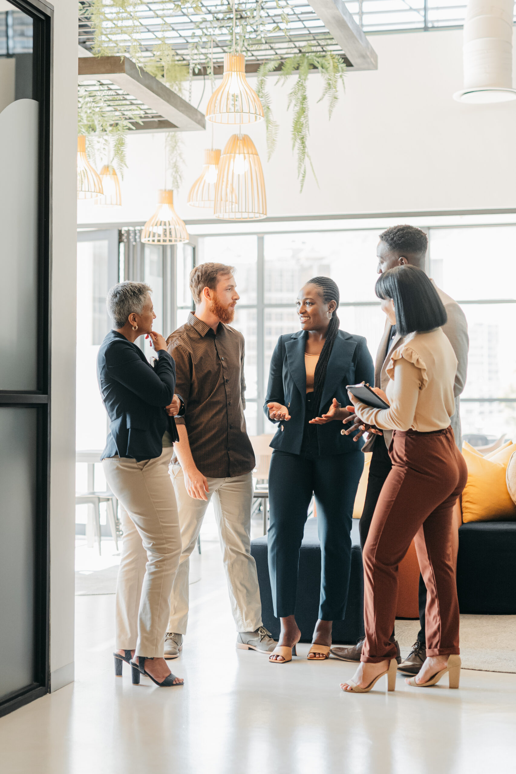 Corporate team standing in a company lounge having discussion about creative project. Diversity, staff and professional people planning meeting in office building. Work friends having a conversation.